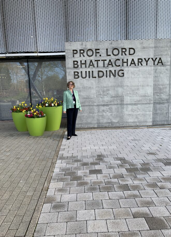 Jan standing outside the Lord Bhattacharya building at Warwick University in dark trousers and a green jacket.
